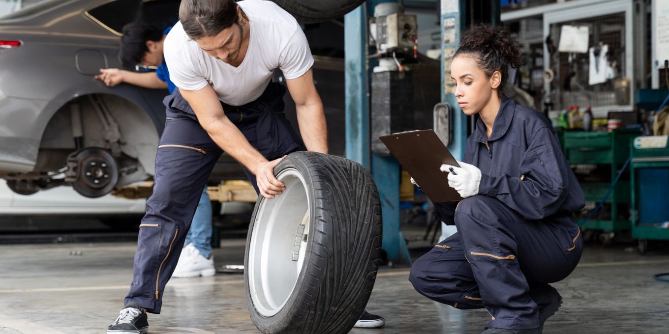 Gruppe von Mechaniker-Fahrzeugservice-Wartung, die Radreifen in der Werkstatt untersucht 1800x900