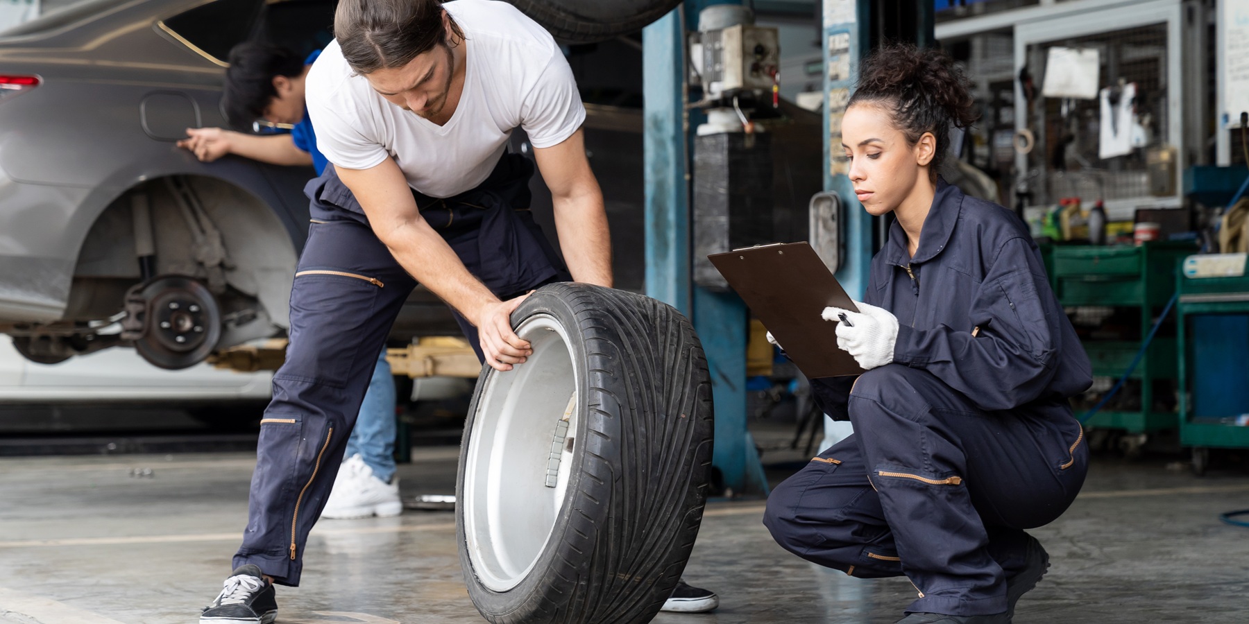 Gruppe von Mechaniker-Fahrzeugservice-Wartung, die Radreifen in der Werkstatt untersucht 1800x900